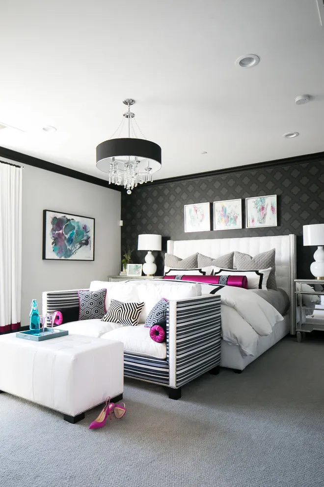 A pale bed with pink accent cushions sits against a dark patterned wall beside striped chairs