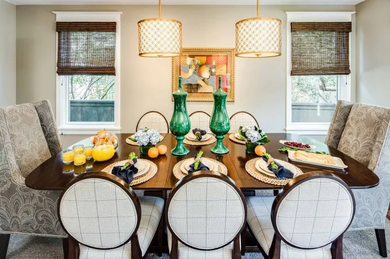 Dining room with a dark wood table, rounded pale side chairs, larger patterned end chairs and two light patterned pendants