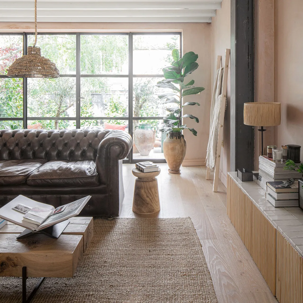 A dark leather sofa sits beside a woven rug and a low timber table.