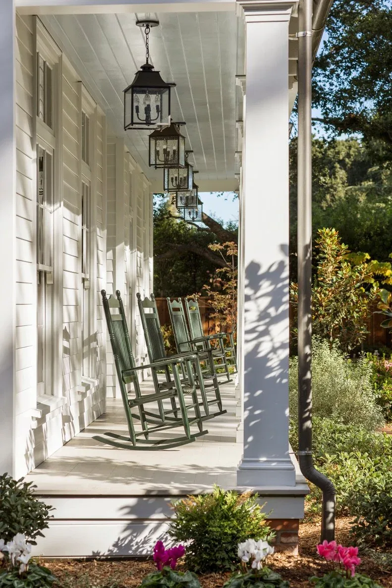 Long white porch with pale green rocking chairs, hanging lanterns and planting beside the columns