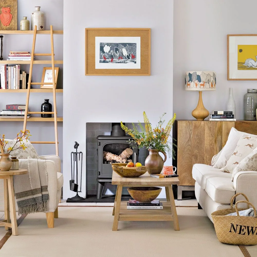 Wooden shelves and a cabinet surround a dark stove beside pale chairs and a wooden coffee table