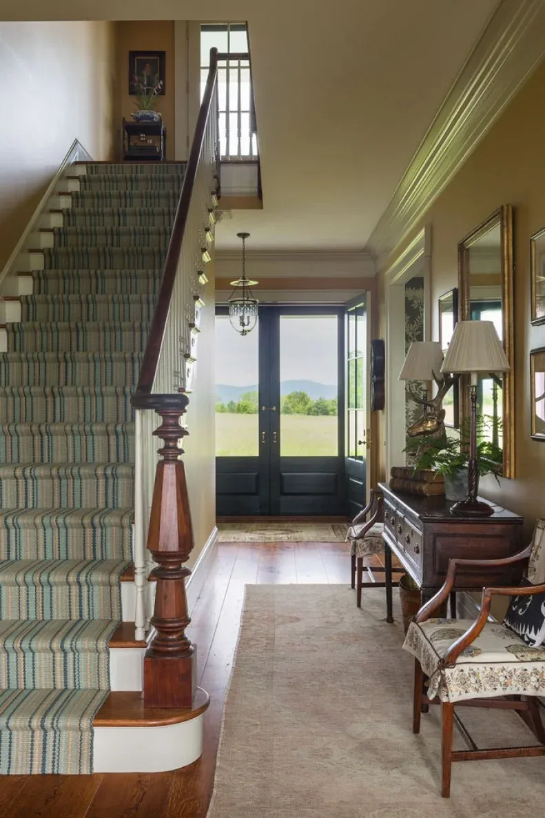 Small clear candle lantern in long traditional entry with dark double door, striped stair runner, wood console and matching chairs