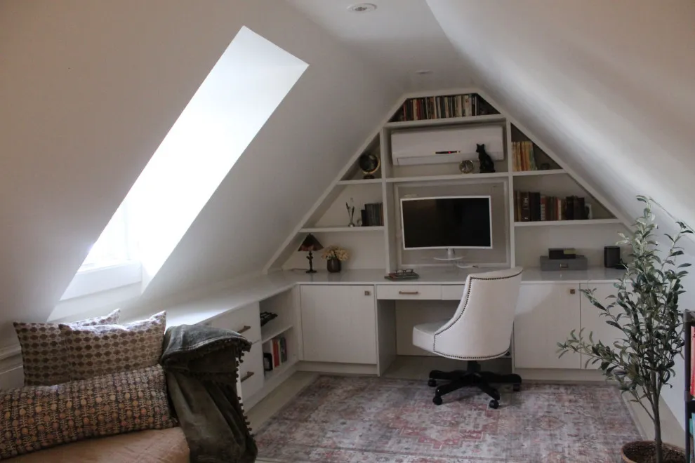 Pale shelving and a desk fit beneath a triangular attic wall and roof window