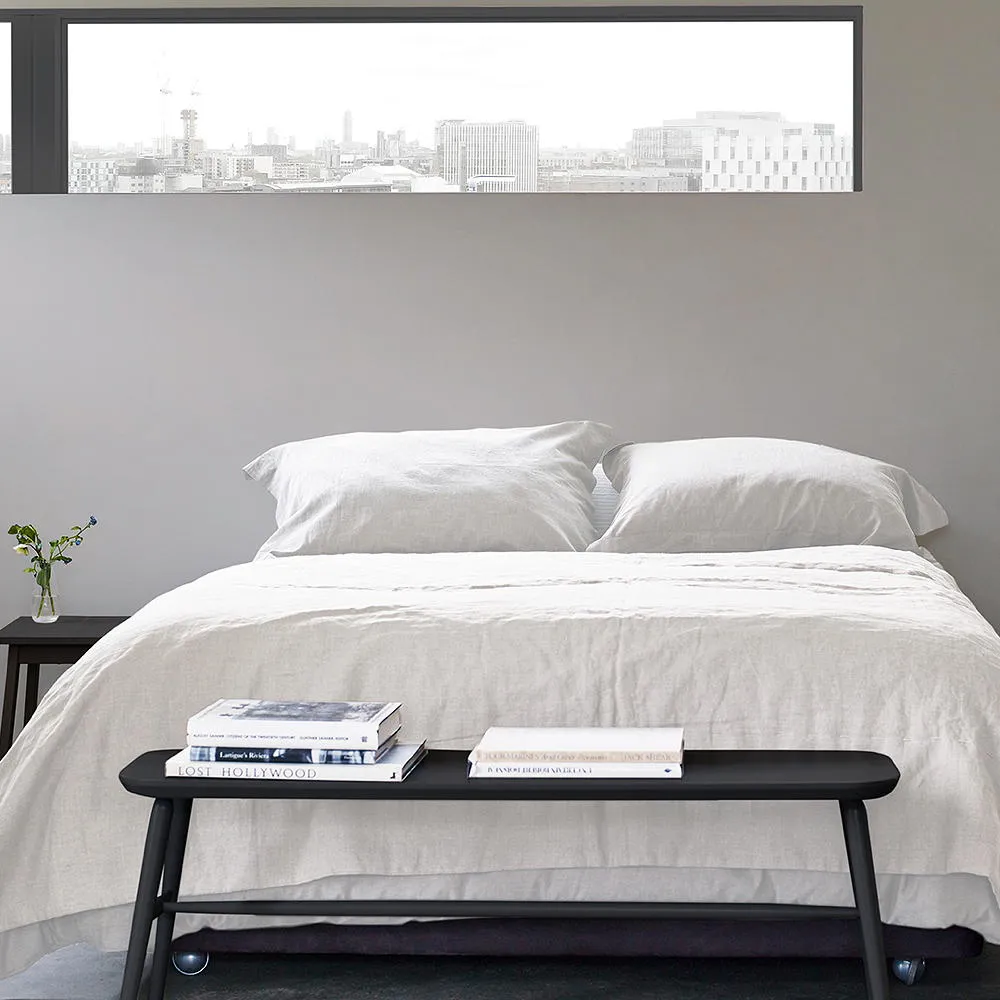 A white bed sits against pale walls with a narrow black bench at the foot