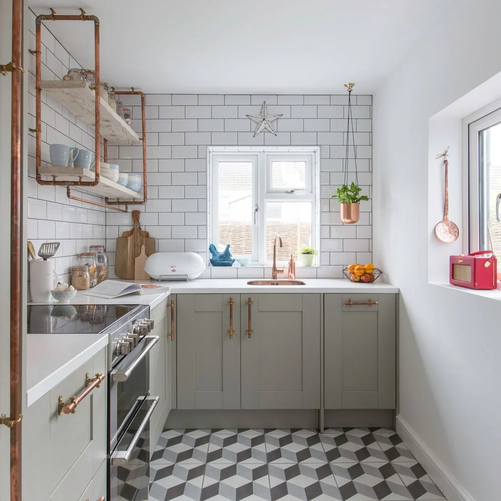 White offset wall tiles surround a kitchen window above pale cabinets and a black-and-gray geometric floor
