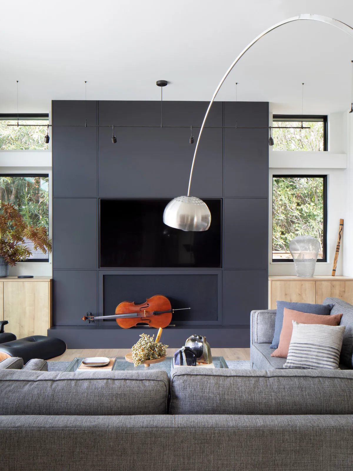 A dark paneled media wall stands behind gray seating and a curved floor lamp.
