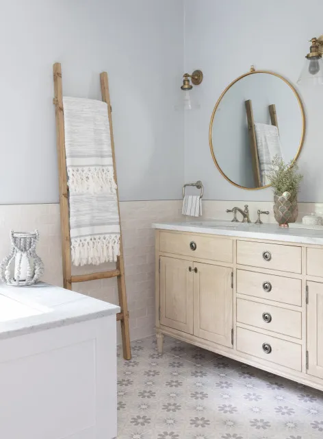 A light timber ladder stands near a pale vanity beneath a round mirror.