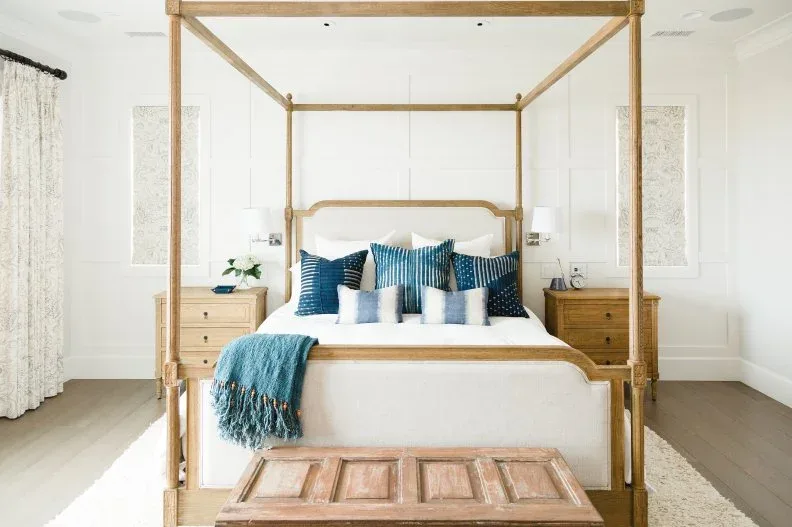 White paneled bedroom with pale wood canopy bed, blue cushions and wood chest at the foot