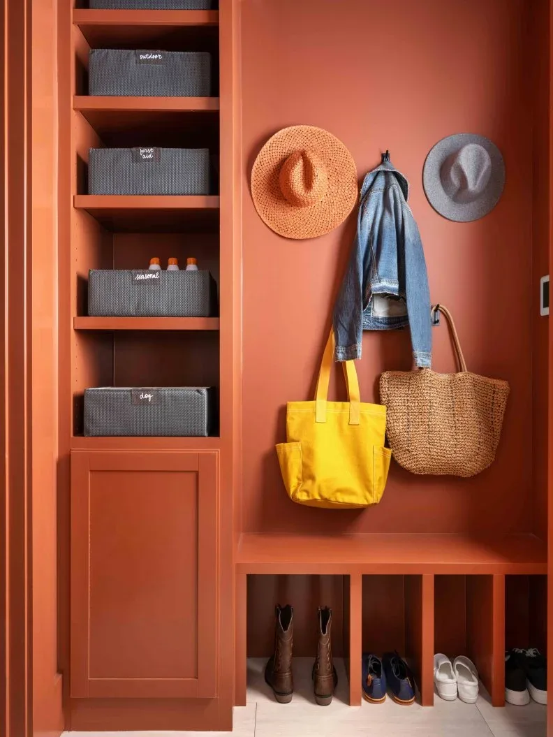 Orange-toned mudroom storage with open shoe cubbies, hat hooks, baskets in side shelves and hanging woven bag.