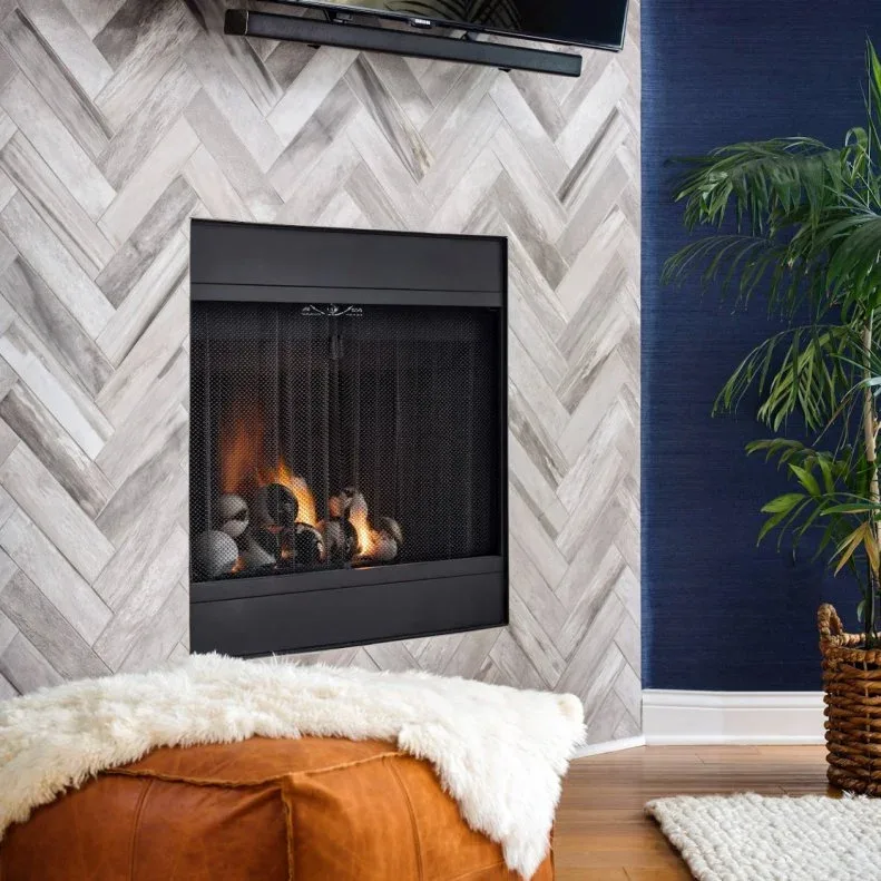 Pale herringbone-tiled fireplace wall beside navy wall, black opening and upholstered footstool