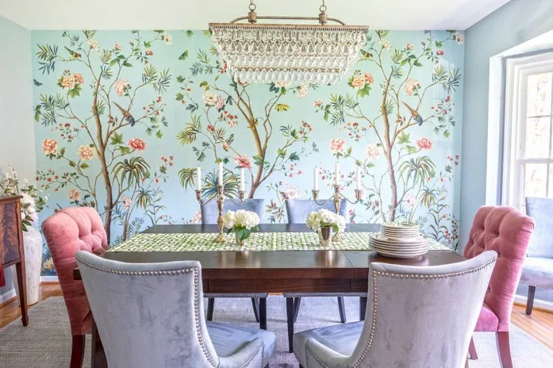 Green patterned runner with low pale flowers, candlesticks and stacked plates on a dark dining table