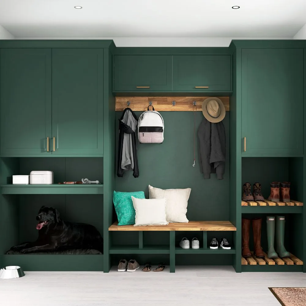Forest green mudroom wall with tall cabinets, a central wooden bench, coat hooks, upper cupboards, shoe shelves, and a dog resting in a side recess.