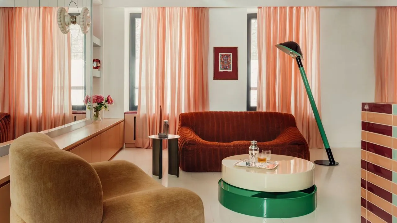 Warm sheer curtains frame a room with red seating, a rounded chair and a green circular table.