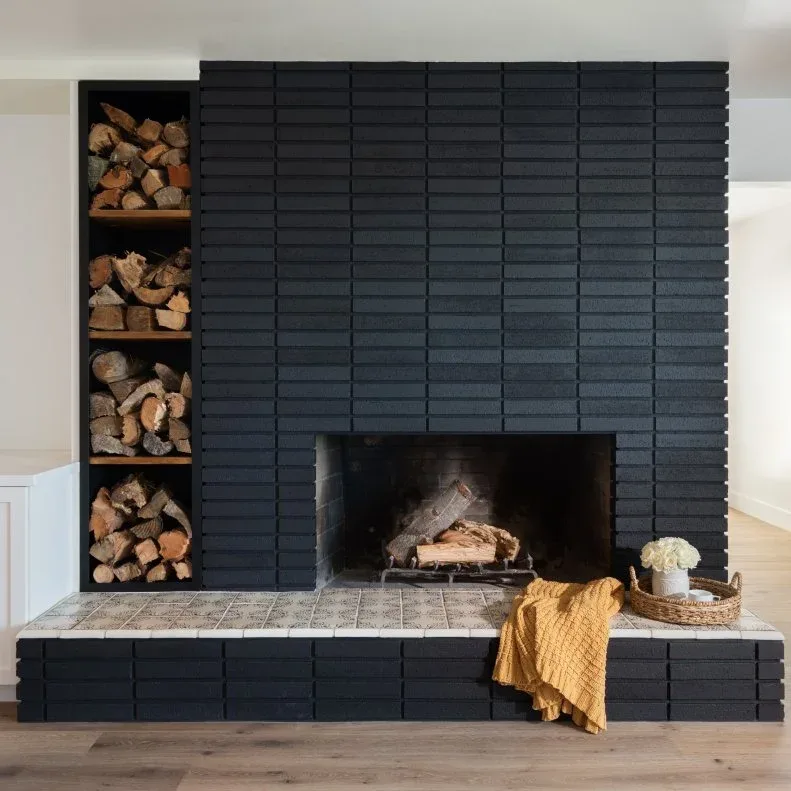 Black brick fireplace with a pale hearth top and a tall divided log niche on the left.