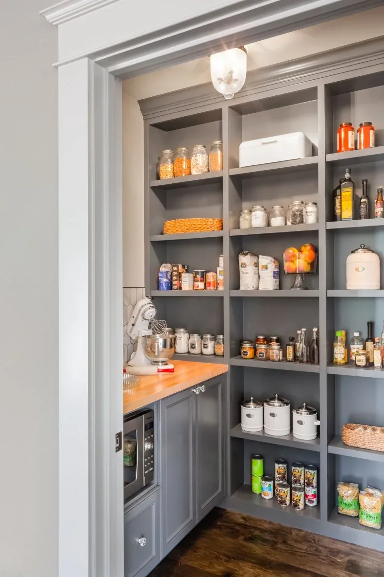 Gray pantry shelving with glass jars, pale canisters, wood counter and lower cabinet with glazed door