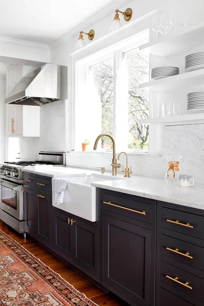 White upper cabinets sit above dark lower doors beside an apron sink and brass faucet