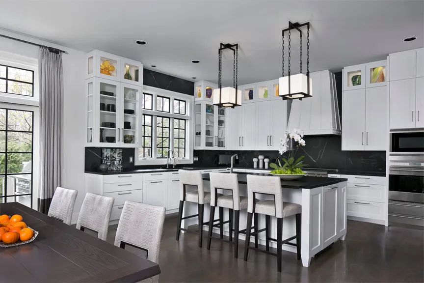 White cabinets with glass doors sit above dark worktops around a bright island
