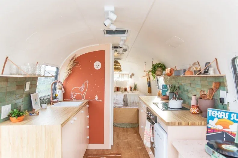 Tiny galley kitchen with green tile, pale counters and a curved coral partition decorated with a simple drawing.