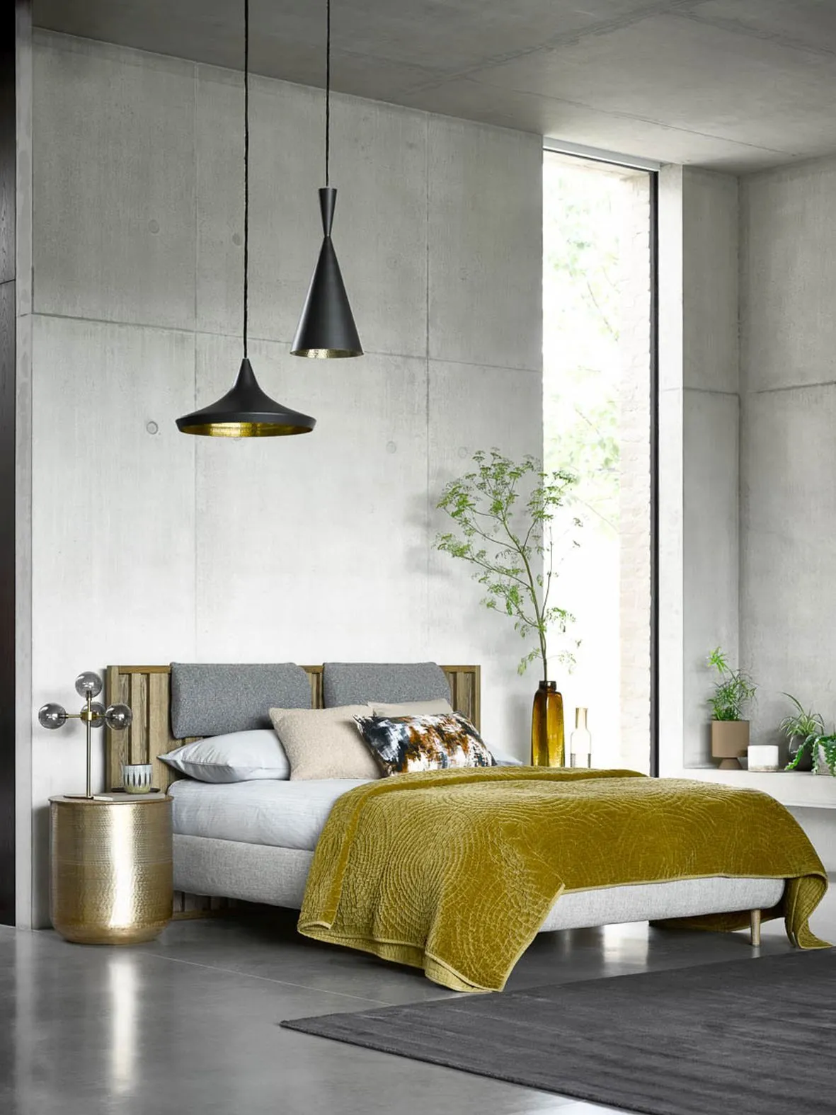 A mustard coverlet sits on a pale bed beneath simple dark pendants.