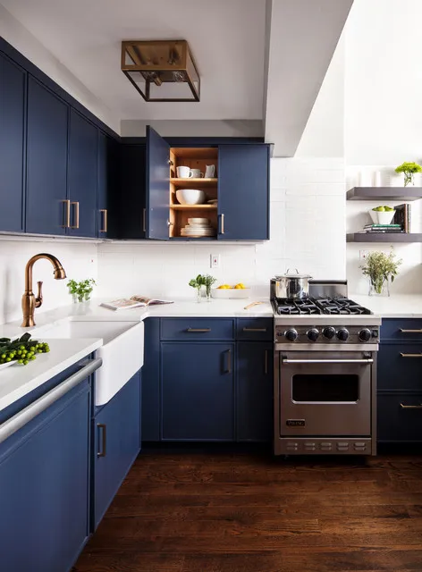 Navy cupboards wrap a compact kitchen below pale counters beside a white apron-front sink, cooker and small wood-lined open cupboard