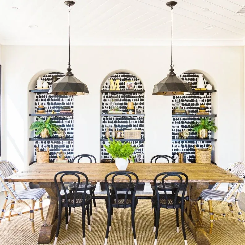 Three arched dining-room recesses with black shelves and black-and-white patterned backs, behind a wooden table, black chairs, pale end chairs, and two dark pendants.