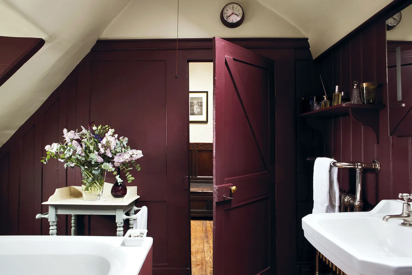 Small bathroom with dark plum paneling, a matching door, white basin and bath edges, wall mirror and a small pale table.