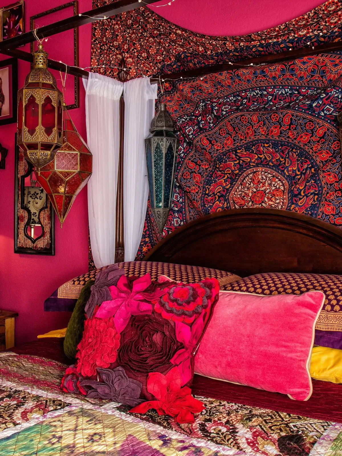 Strong pink bedding sits against deeply patterned walls and a dark timber headboard.
