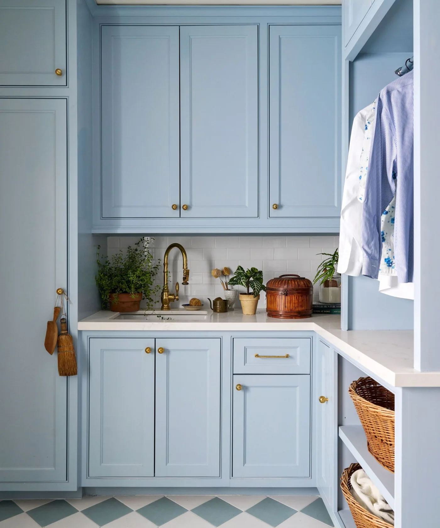 Pale blue utility cupboards with gold-colored hardware, white sink counter, hanging shirts and blue-and-white checked floor