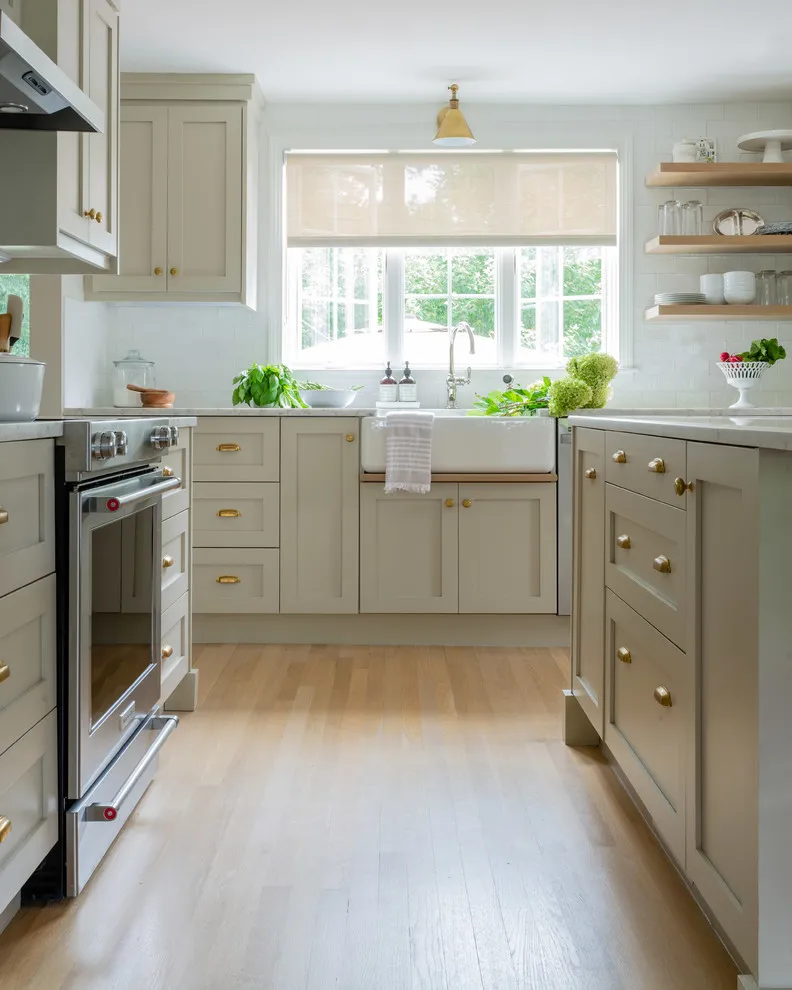 Pale beige cabinets flank a bright sink window with timber shelves to one side