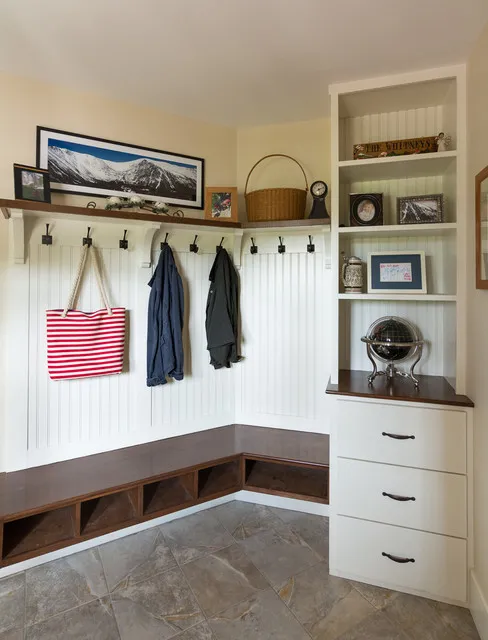 An L-shaped timber bench sits beneath white hooks and open storage beside framed artwork.