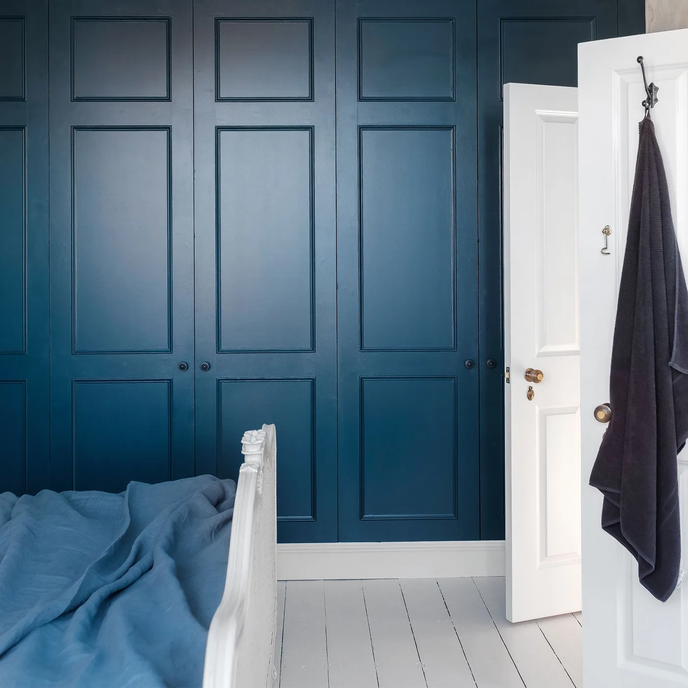 Deep blue paneled bedroom storage and walls beside a white door, pale floorboards, and blue bedding.