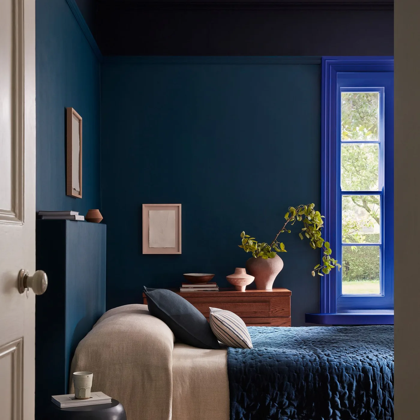 Dark blue bedroom walls and ceiling with brighter blue window trim, a beige bed, and a wooden dresser.