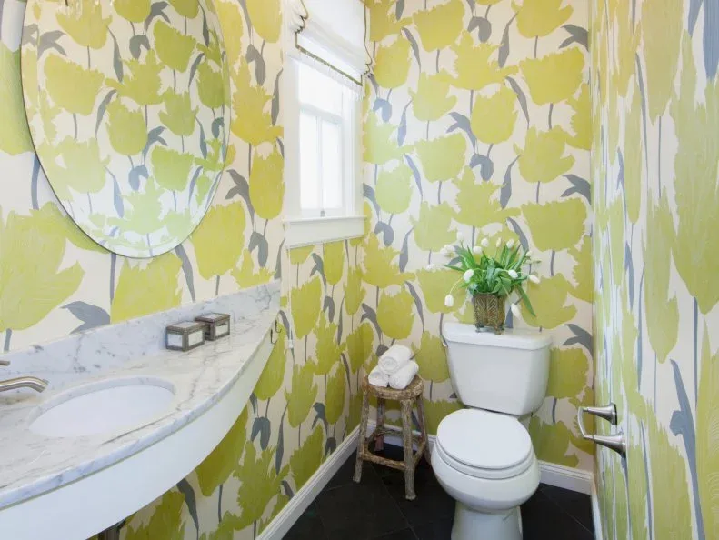 Small powder room with yellow floral wallpaper, curved pale sink counter and white toilet