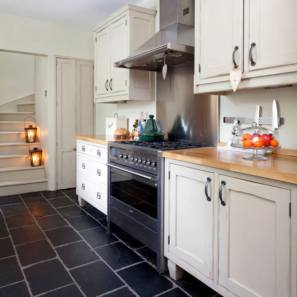 Cream paneled cabinets and wooden counters surround a black range above a dark tiled floor
