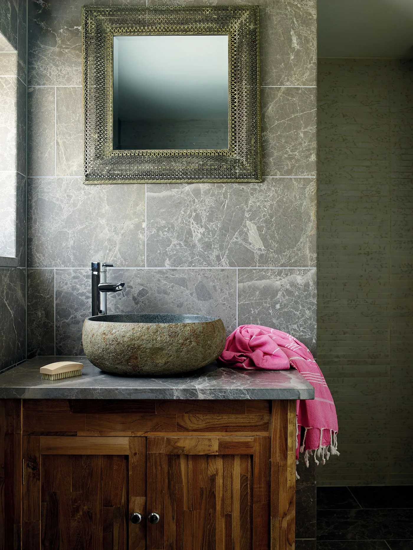 Rounded textured basin on a gray counter above a wood cabinet, with gray veined wall tiles and a framed mirror.