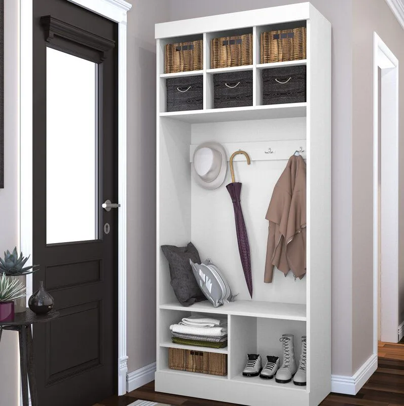 White freestanding hall tree with basket cubbies, hooks and seat beside black glazed front door