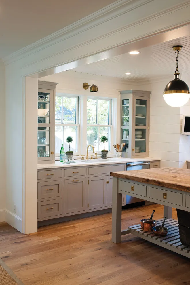 Muted taupe cabinets run below a bank of windows beside a freestanding wooden worktable