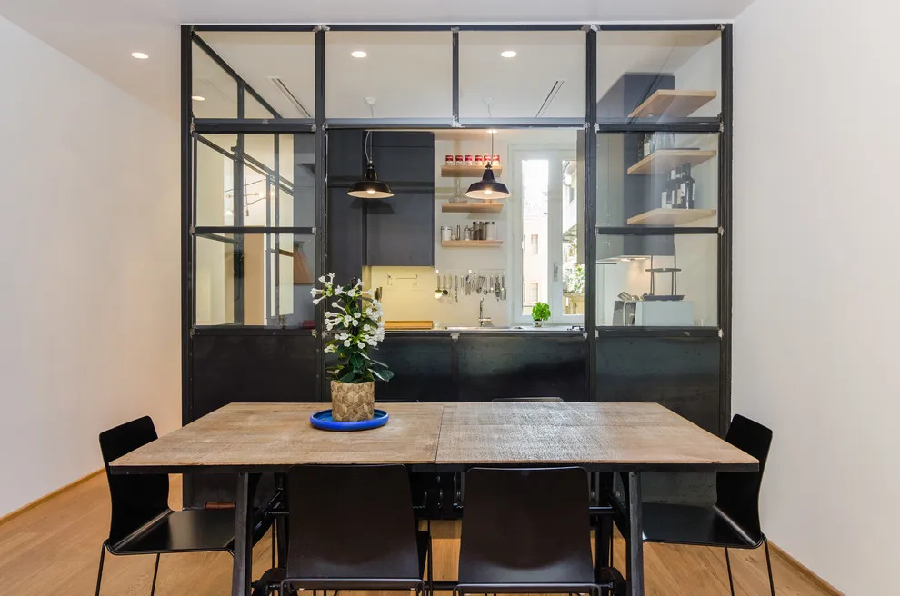 A timber dining table sits in front of a black-framed glass partition