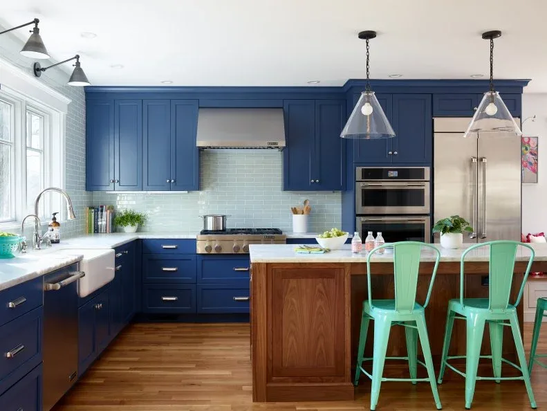 Blue kitchen cabinets with pale blue-green rectangular backsplash tiles, white counters, a wooden island and light green dining chairs.