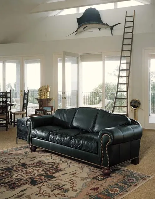 A black rolled-arm leather sofa sits beneath a pale high ceiling beside glazed doors and a patterned rug.