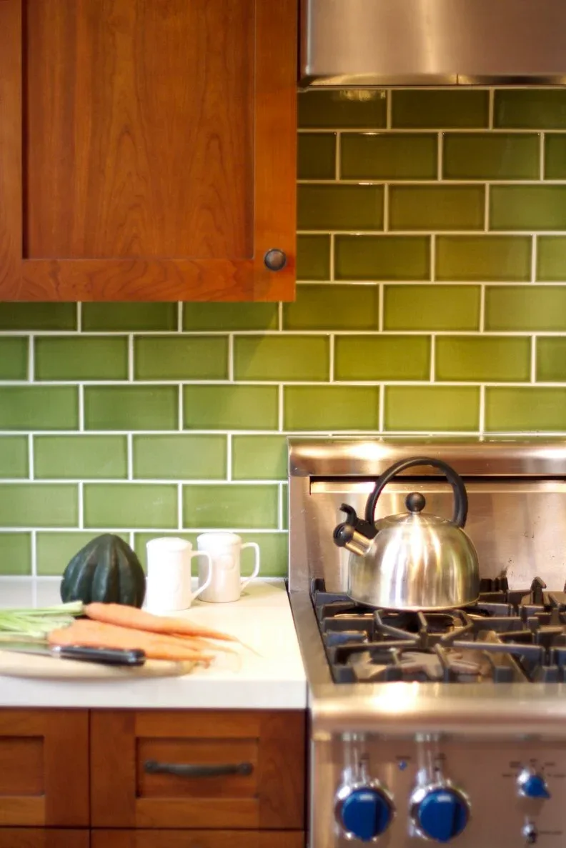 Warm wooden kitchen cabinets beside a cooker with glossy green rectangular backsplash tiles laid in offset rows with light grout.