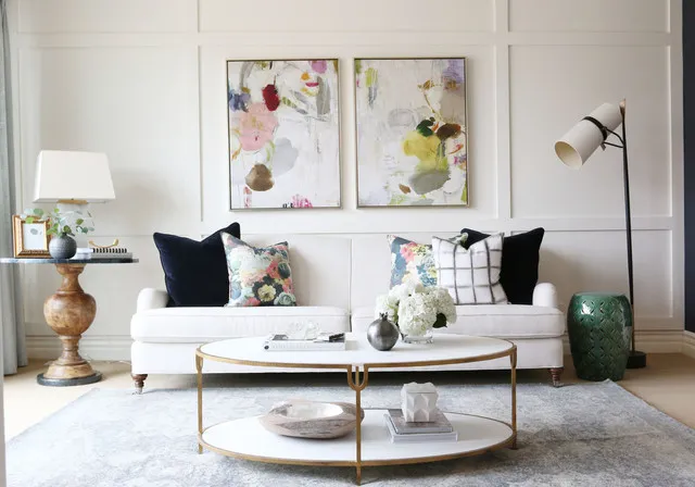 A white sofa stands beneath colorful artwork with darker cushions and a slim table.