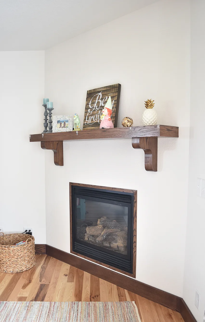 White angled fireplace with a dark wood mantel on brackets, teal candles and small decorations.