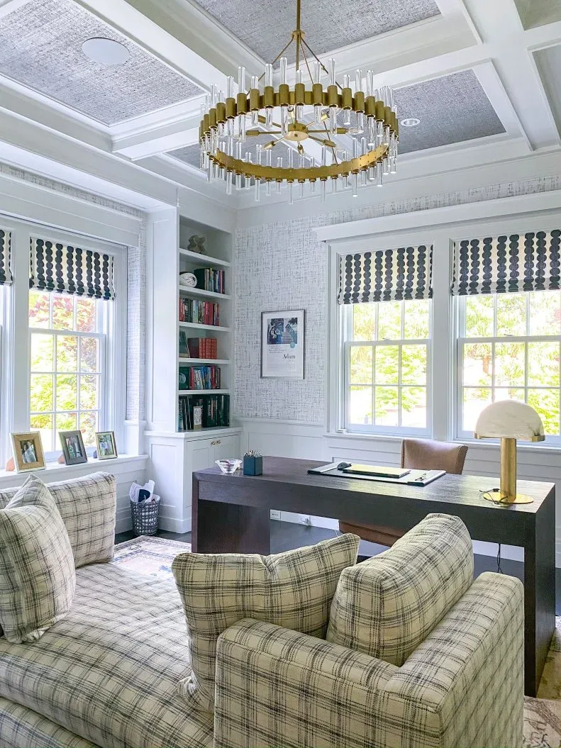 Dark desk and plaid seating beneath a gold-toned ring chandelier with clear rods in a pale office.