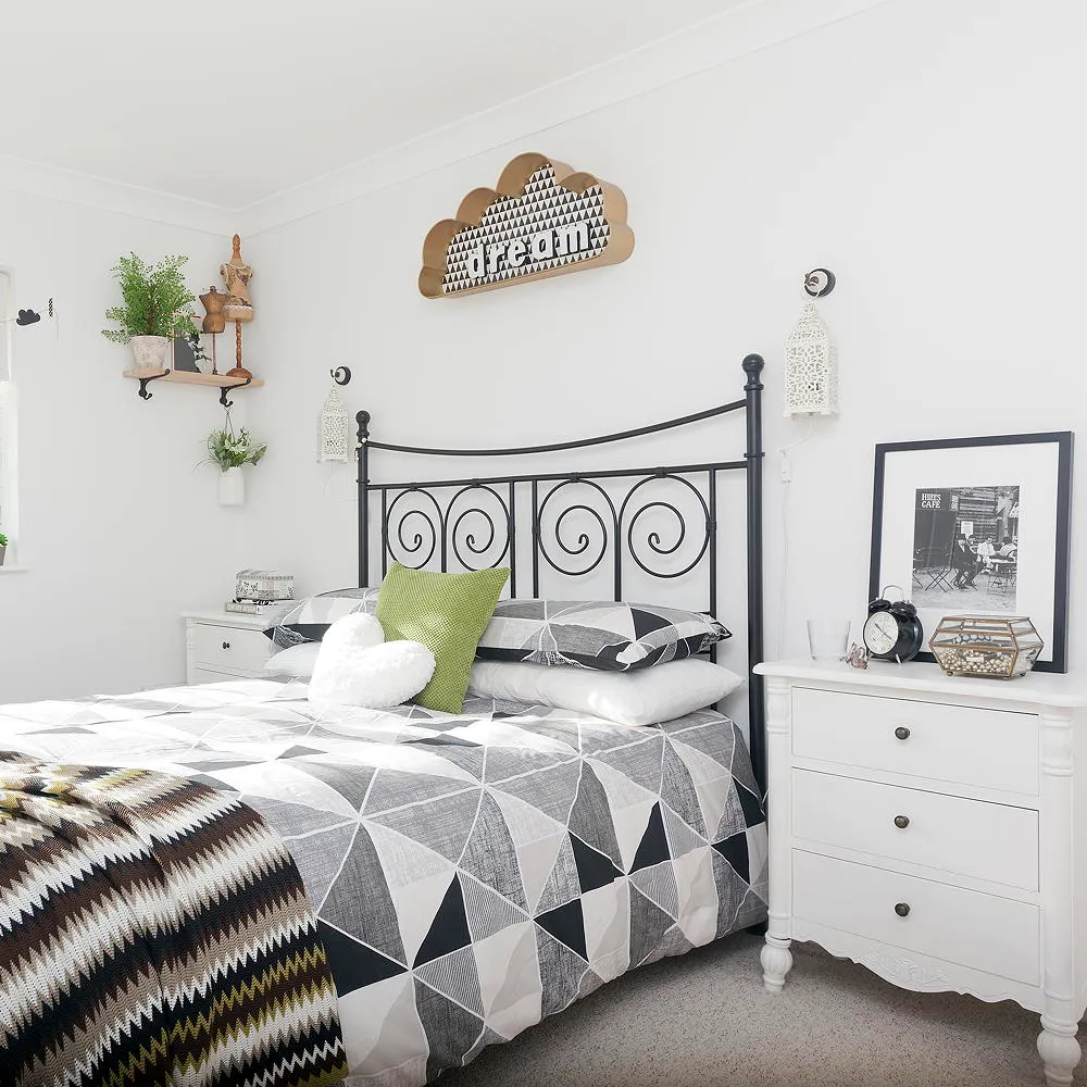 A black metal bed carries gray-and-white geometric bedding beside white walls