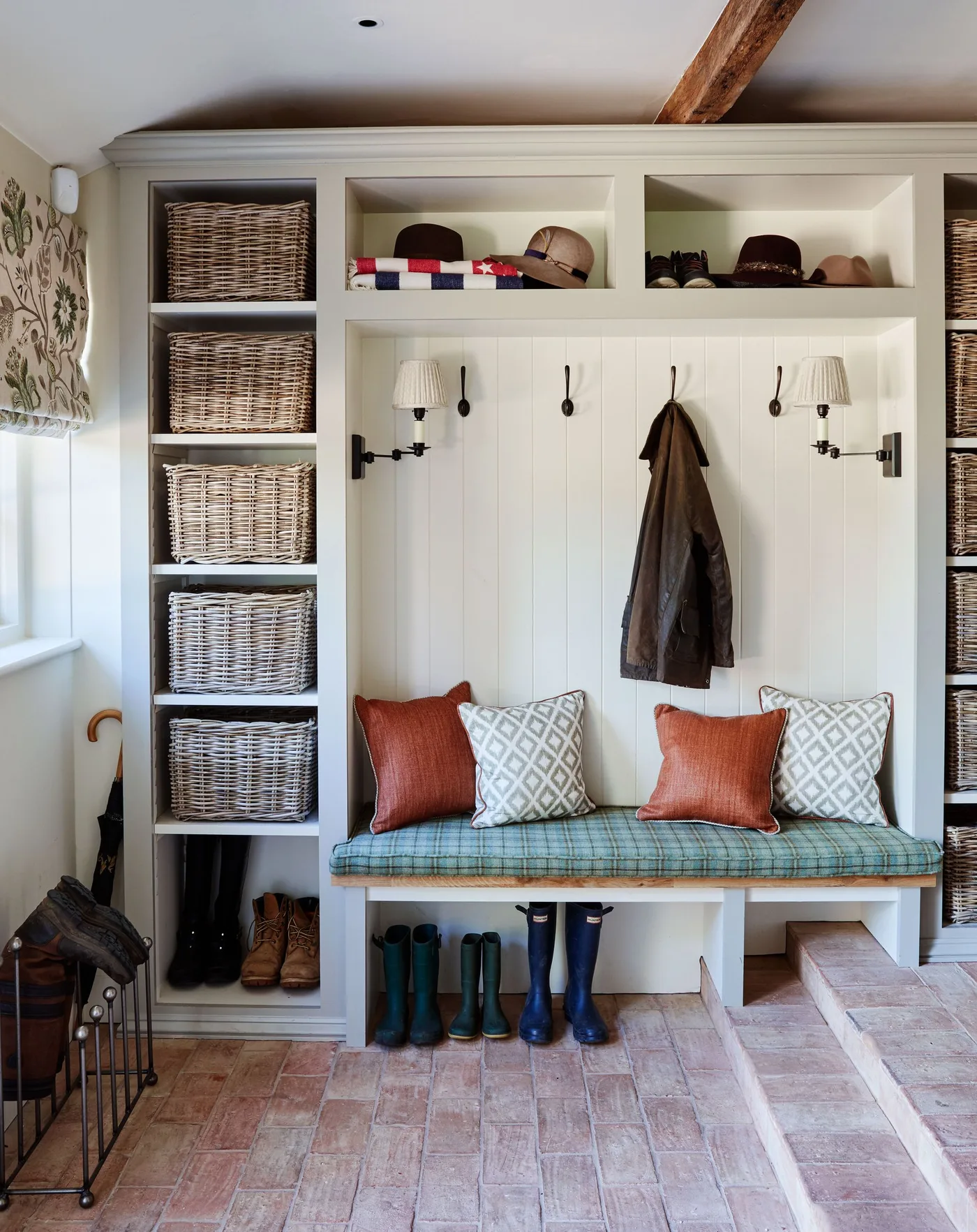 Pale entry storage with a checked bench, rust cushions, tall basket columns, wall hooks and boots below