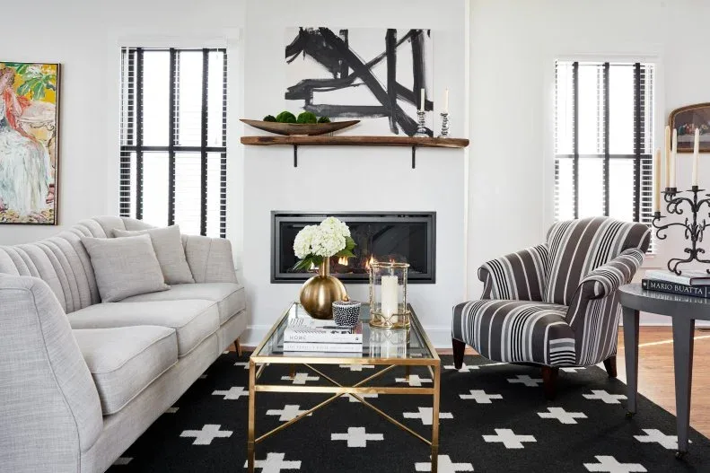 White living room with dark fireplace insert, black and white cross-pattern rug and striped armchair