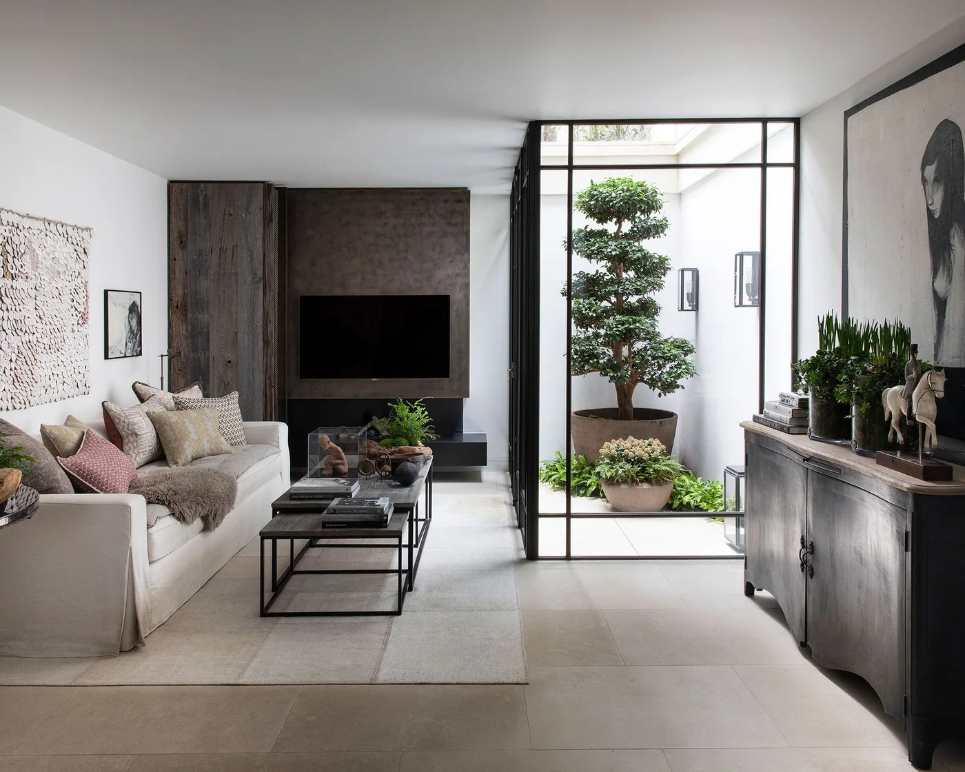 A television sits on a dark wall beside a tall black-framed opening and pale sofa with a narrow dark table