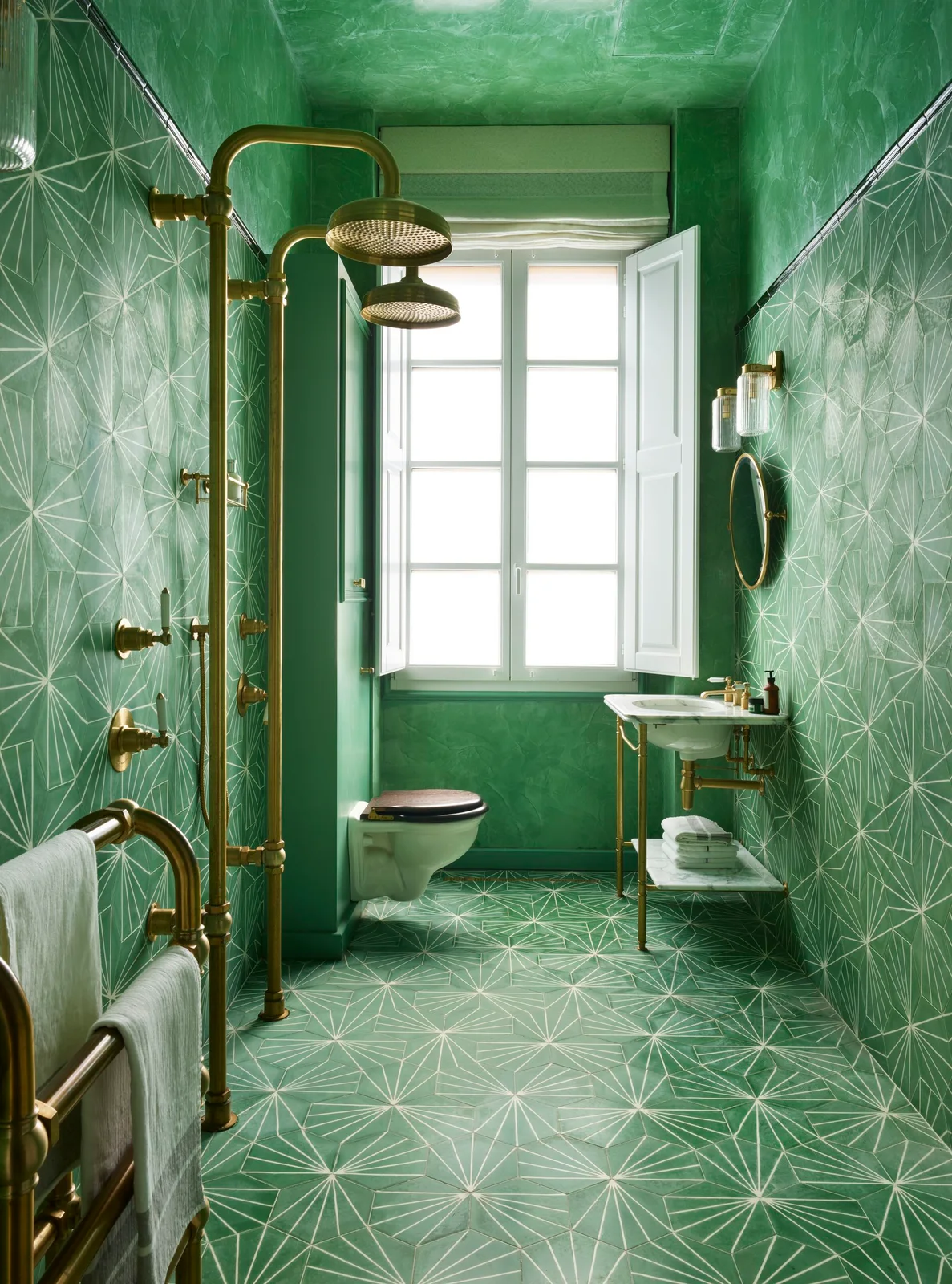 Green patterned tiles cover shower walls and floor beneath a green ceiling beside gold-toned shower fittings and a small basin