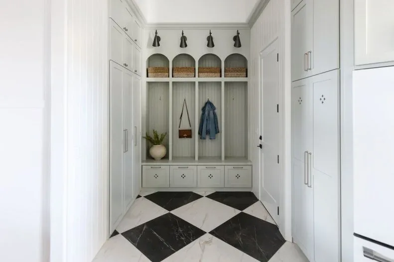 White mudroom with arched coat cubbies, baskets, lower bench drawers, tall side cabinets and black and white checked floor.